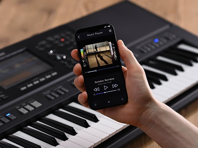 Yamaha Arranger Workstation PSR-SX920 e uma mão a segurar um smartphone com um ecrã de leitor de música