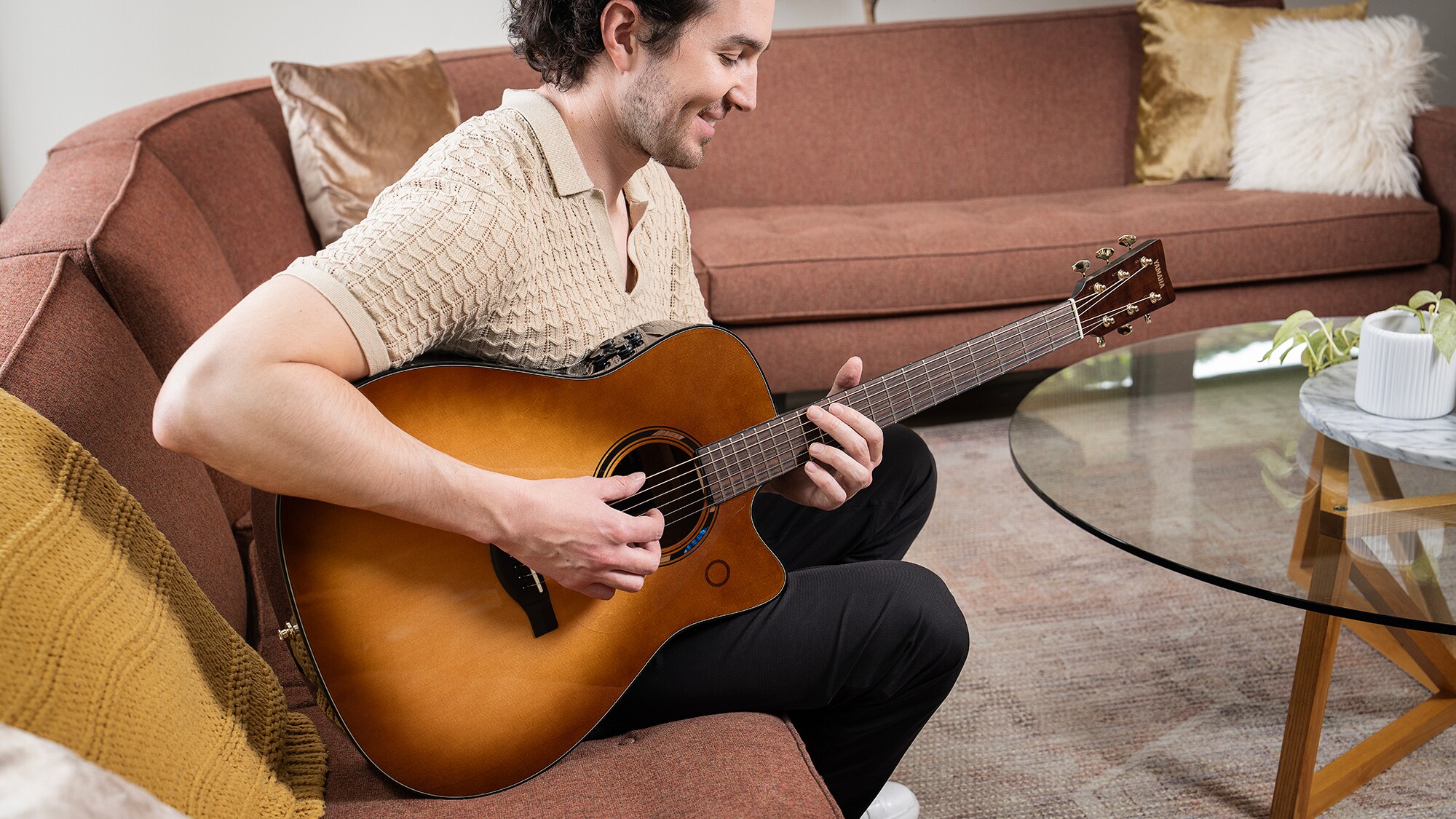 Um homem sentado num sofá na sala de estar a tocar uma guitarra acústica TAG3 C
