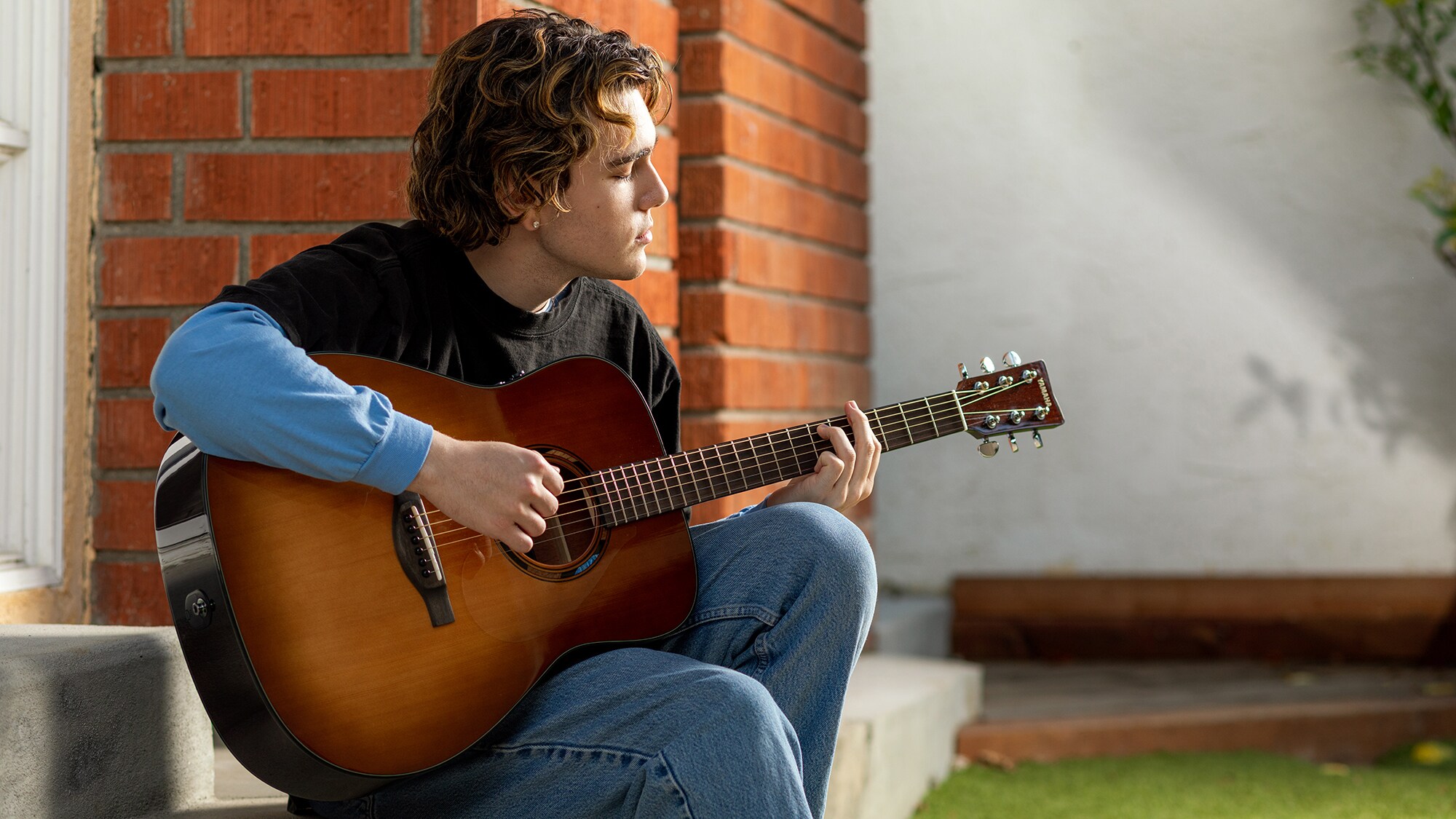 Um homem a tocar uma guitarra acústica TAG1 E ao ar livre