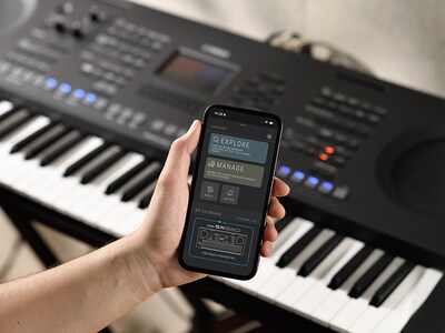PSR-SX620 e uma mão a segurar um smartphone com o ecrã da aplicação oficial da Yamaha "Expansion Explorer".