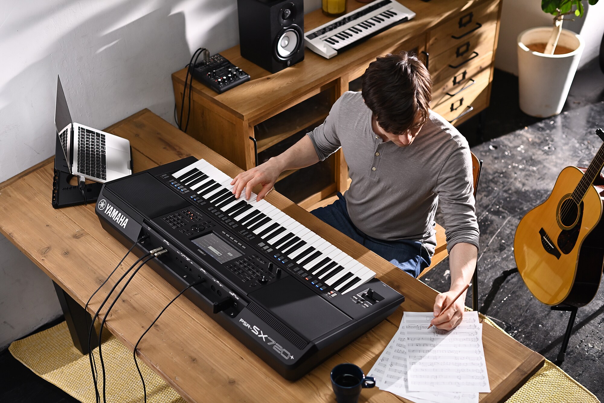 Fotografia de uma pessoa a escrever numa partitura enquanto toca o Yamaha Arranger Workstation PSR-SX720+