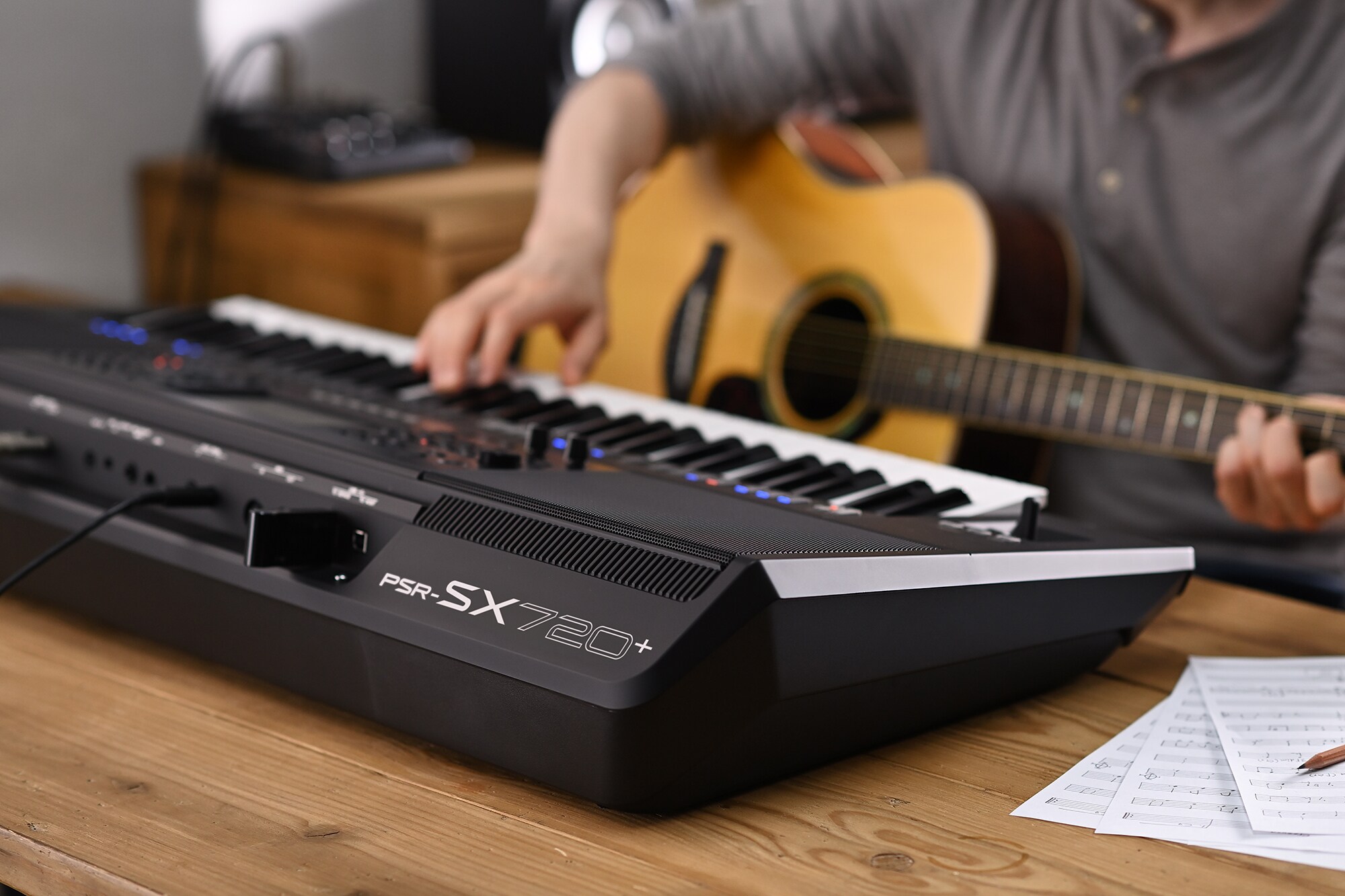 Fotografia de uma pessoa a tocar o Yamaha Arranger Workstation PSR-SX720+ enquanto segura uma guitarra
