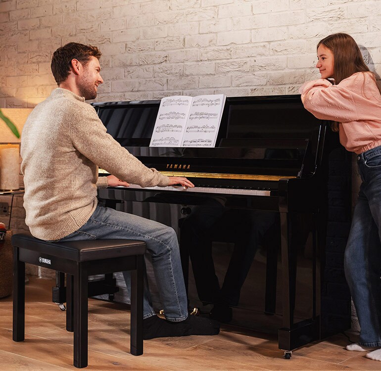 Uma mãe e a sua filha desfrutam ao tocar o piano vertical da Série B