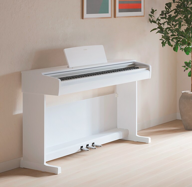 Uma sala de estar com um piano ARIUS em branco, plantas de interior e um sofá, harmoniosamente integrado no interior