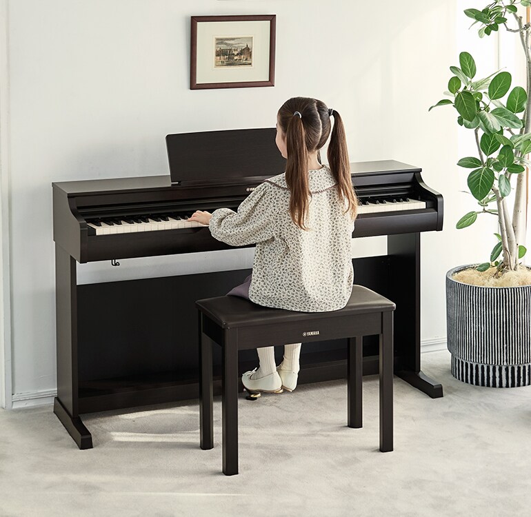 Uma jovem a estudar num piano ARIUS numa sala de estar.