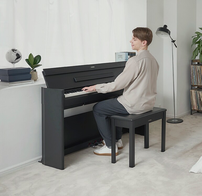 Um homem a tocar um piano ARIUS num quarto, num ambiente descontraído.