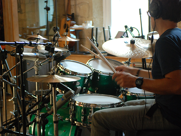 A man playing on a drum set with a microphone set up for recording